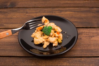 tavuk, bir kaşık ile siyah bir tabak ve bir tabak brokoli. ahşap rustik masa