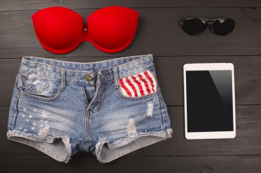 Bayan aksesuarlar yaz: kırmızı sutyen, kot şort, tablet, ahşap arka plan üzerinde güneş gözlüğü