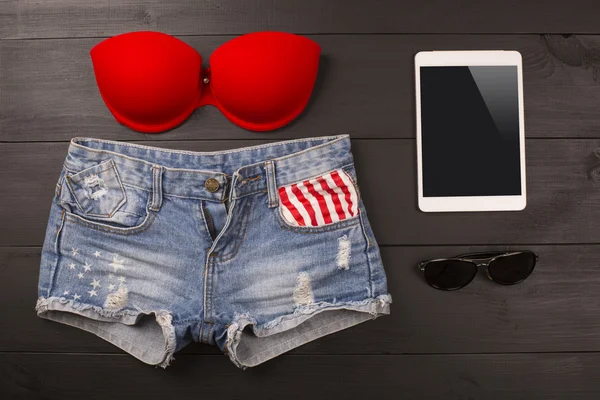 Acessórios femininos de verão: sutiã vermelho, calções jeans, tablet, óculos de sol sobre fundo de madeira — Fotografia de Stock