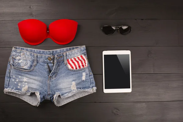 Acessórios femininos de verão: sutiã vermelho, calções jeans, tablet, óculos de sol sobre fundo de madeira — Fotografia de Stock