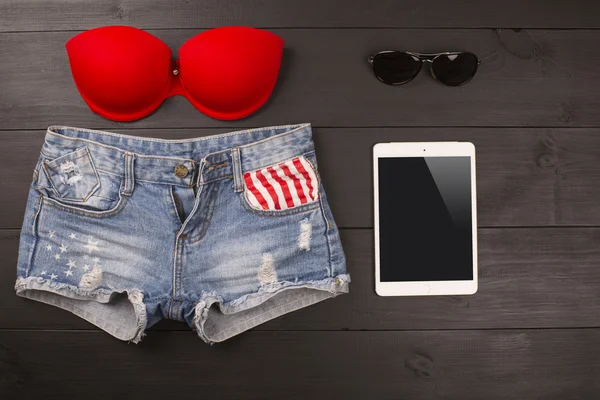 Acessórios femininos de verão: sutiã vermelho, calções jeans, tablet, óculos de sol sobre fundo de madeira — Fotografia de Stock