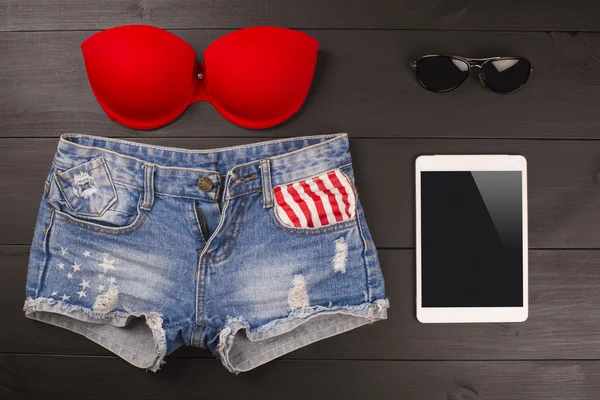 Acessórios femininos de verão: sutiã vermelho, calções jeans, tablet, óculos de sol sobre fundo de madeira — Fotografia de Stock