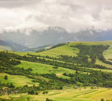 Ağır yağmurlu bulutlar altında yeşil tepe üzerinde dağ köyü
