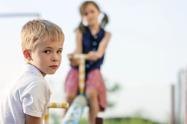 Kinderen spelen op de schommel. Jongen in focus en meisje wazig achter. — Stockfoto