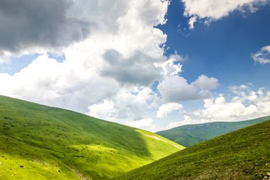 Yeşil çimenli tepeler ve beyaz kabarık bulutlu mavi gökyüzü