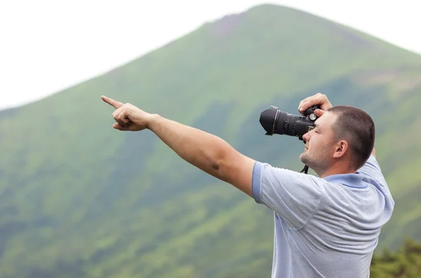 Photographer with a camera  taking picture of mountains pointing