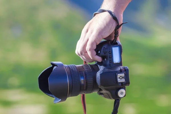 Mano di un uomo che tiene una fotocamera digitale professionale su un gre sfocato — Foto Stock