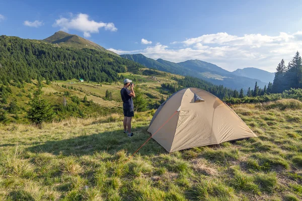 Фотограф-турист, стоящий возле палатки и фотографирующий гору — стоковое фото