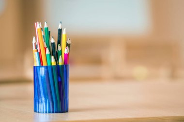 Hafif fotokopi arkaplanındaki plastik sürahiye yerleştirilmiş tahta renkli çizim kalemleri.