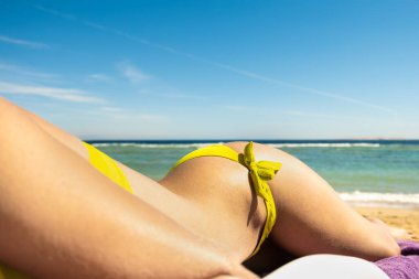 Deniz kıyısında güneş banyosu yaparken plaj sandalyesinde uzanan genç bir kadının kalçasına ve omzuna yakın çekim.