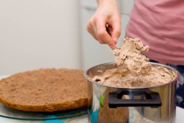 Evde kek pişirme süreci. Çikolatalı bisküvinin üzerine kadın el kreması dök. Mutfak ve lezzetli tatlı konsepti.