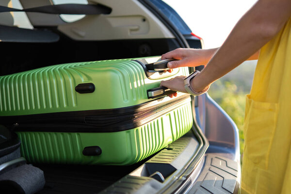 Молодая женщина берет зеленый чемодан из багажника машины. Концепция путешествий и отдыха.