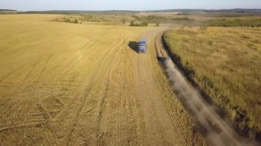 Toprak yolda hızla giden arabanın yukarıdan görünüşü ardında toz bulutu bırakıyor..