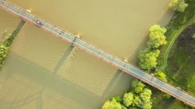 Yeşil kırsal bölgedeki çamurlu geniş nehir üzerindeki dar bir köprünün havadan görüntüsü..