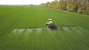 İlkbaharda büyük yeşil alana kimyasal böcek ilacı püskürten bir traktörün hava görüntüsü..