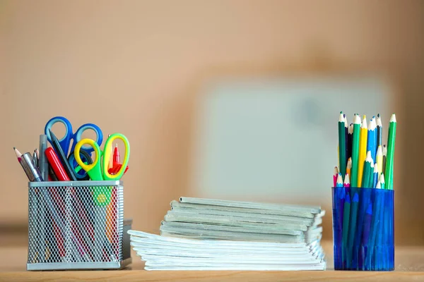 Stack of notebooks, colorful drawing pencils and stationery arrangement on copy space background.