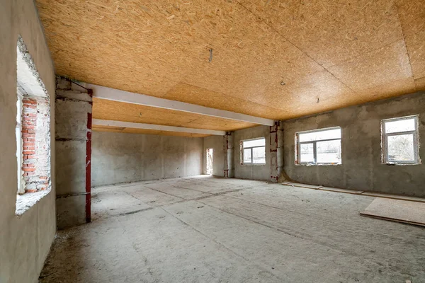 Unfinished apartment or house big loft room under reconstruction. Plywood ceiling, plastered walls, window openings, cement floor. Construction and renovation concept.