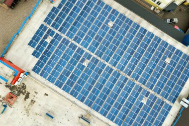 Sanayi binasının çatısına monte edilmiş mavi fotovoltaik panelleri olan güneş enerjisi santralinin hava görüntüsü.