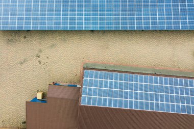 Sanayi binasının çatısına monte edilmiş mavi fotovoltaik panelleri olan güneş enerjisi santralinin hava görüntüsü.