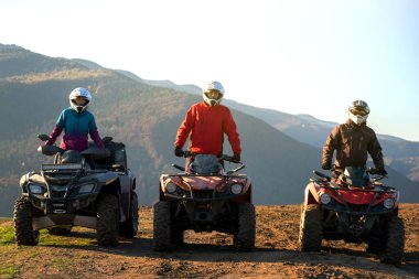 Koruyucu kasklı mutlu sürücüler günbatımında ATV dörtlü motorsiklet sürmenin keyfini çıkarıyorlar..
