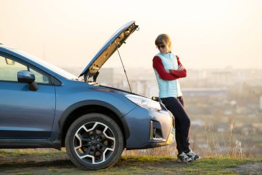 Kaputu patlamış, bozuk bir arabanın yanında duran genç bir kadın aracıyla sorun yaşıyor. Otomatik arıza dışında yardım bekleyen kadın sürücü.