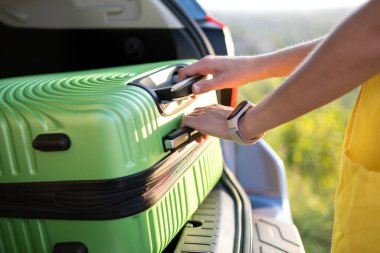 Arabanın bagajından yeşil bavulu alan kadına yaklaş. Seyahat ve tatil kavramı.