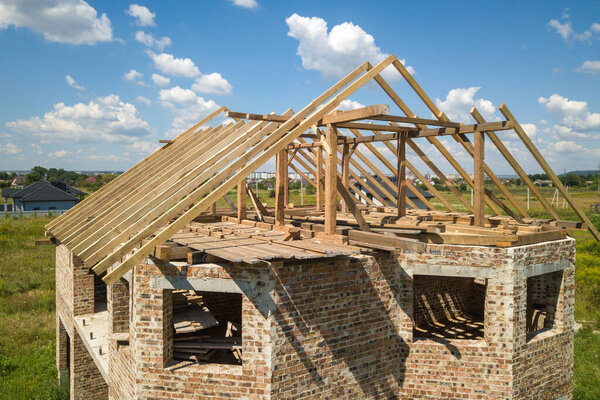 Aerial view of unfinished house with wooden roof frame structure under construction.