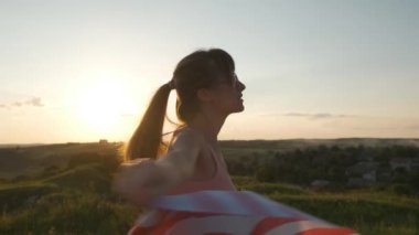 Gün batımında dışarıda Amerikan bayrağıyla poz veren mutlu genç kadın. Amerika 'nın bağımsızlık gününü kutlayan pozitif kız. Uluslararası Demokrasi Günü.