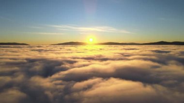 Sarı günbatımında beyaz kabarık bulutların üzerinden hava manzarası.