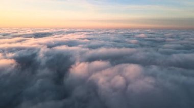 Üzerinde mavi gökyüzü olan beyaz yoğun bulutların üzerinde parlak sarı günbatımının havadan görünüşü.