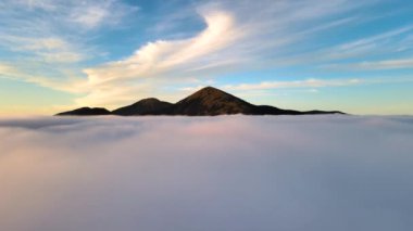 Ufuktaki uzak dağlarla beyaz kabarık bulutların üzerinde sarı günbatımının havadan görünüşü.