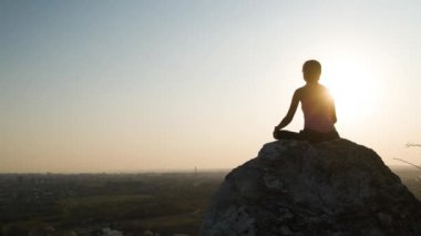 Genç, rahat bir kadın büyük bir taşın üzerinde oturmuş sıcak bir yaz gününün tadını çıkarıyor. Gün batımında meditasyon yapan ve dinlenen bir kız..