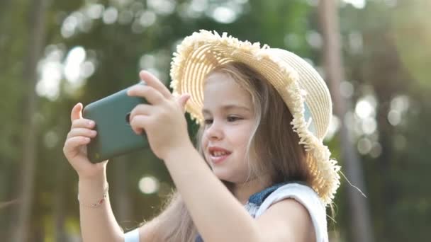 Glücklich Lächelndes Kindermädchen Das Sommer Draußen Mit Seinem Handy Zusieht — Stockvideo