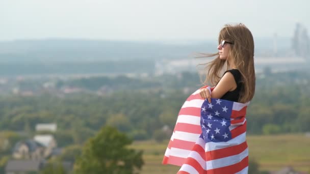 年轻而快乐的女人 长长的秀发迎风飘扬 飘扬着美国国旗 飘扬在户外 享受夏日的温暖 — 图库视频影像