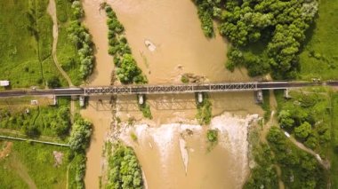 Baharda sağanak yağış sırasında kirli nehir üzerinde çamurlu suyla demiryolu metal köprüsünün havadan görünüşü.