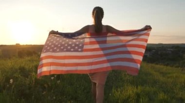 Gün batımında ABD bayrağıyla gezen genç bir kadın. Amerika 'nın bağımsızlık gününü kutlayan pozitif kız. Uluslararası Demokrasi Günü.