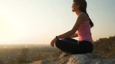 Genç, rahat bir kadın büyük bir taşın üzerinde oturmuş sıcak bir yaz gününün tadını çıkarıyor. Gün batımında meditasyon yapan ve dinlenen bir kız..