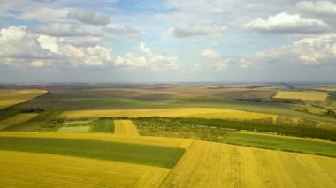 Sarı yamalı tarım arazileri ve beyaz bulutlu mavi gökyüzü olan havadan kırsal alan..