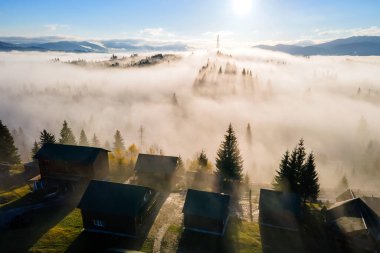 Güneşin doğuşuyla sisli dağlarda tepedeki küçük köy evlerinin hava manzarası..