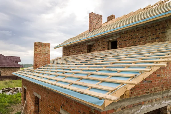 Aerial view of a brick house with wooden roof frame under construction.