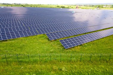 Yeşil alandaki güneş enerjisi santralinin koruyucu tel örgülü havadan görüntüsü. Temiz ekolojik enerji üretmek için elektrik panelleri.