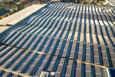 Sanayi binasının çatısına monte edilmiş birçok voltaik güneş panelinin hava görüntüsü.