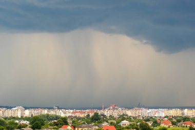 Kara fırtınalı bulutlarla kapkara bir manzara Yazın uzak kasaba binalarının üzerine sağanak yağmur yağıyor.