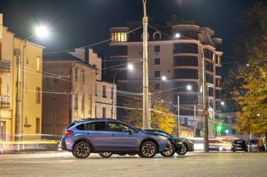 Gece vakti aydınlık şehir sokağına park edilmiş mavi bir araba..