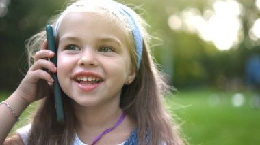 Mutlu küçük kız yaz parkında cep telefonuyla konuşuyor..