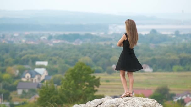 穿着黑色短裙站在山顶上享受夏日温暖的长发女子 — 图库视频影像