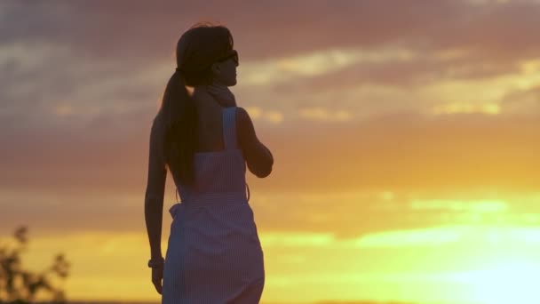 Tmavá silueta mladé ženy stojící na kameni a užívající si výhled na západ slunce v létě.