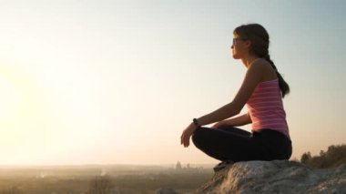 Genç, rahat bir kadın büyük bir taşın üzerinde oturmuş sıcak bir yaz gününün tadını çıkarıyor. Gün batımında meditasyon yapan ve dinlenen bir kız..