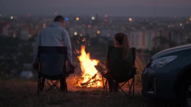 Geceleri yanan sarı kamp ateşinin önünde kamp sandalyelerinde dinlenen mutlu çift..
