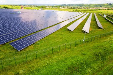 Yeşil alandaki güneş enerjisi santralinin koruyucu tel örgülü havadan görüntüsü. Temiz ekolojik enerji üretmek için elektrik panelleri.